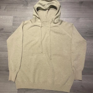 Merinoull hoodie - Säljer en stilren beige hoodie med huva och dragsko. Tröjan har långa ärmar och ribbade muddar vid ärmslut och nederkant. Perfekt för en avslappnad look.