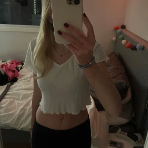 Vit croppad t-shirt - Säljer en vit croppad t-shirt med v-ringning och korta ärmar. Perfekt för en avslappnad stil. 