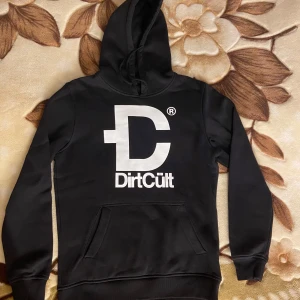 Svart Dirtcült hoodie NYSKICK - stl M - Helt ny svart Dirtcült hoodie i svart färg som aldrig kommit till användning. Endast prislapp borttagen. Trycket är helt, inga lösa trådar, etc. Exceptionellt skick! Oversize. Stor luva. Manlig modell. Stor ficka. Varm. Mjuk insida. Storlek: M. Nypris: 798 kr 