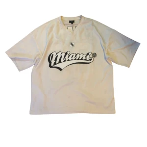 Oversized Jersey - Snygg vit Jersey med Miami-tryck i svart på framsidan och stort '83' på baksidan. Den har en oversized passform och i ett fint skick, dock så finns det fläckar på den som kanske går bort men det är ju en vit/beige tröja så de e ju enkelt att få någon fläck på men dem kan nog gå bort i tvätten.