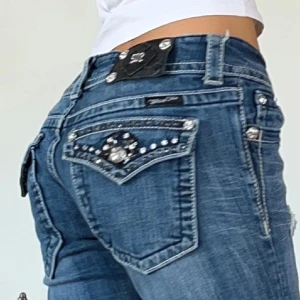 Blå jeans med detaljer från Miss Me - Snygga blå jeans från Miss Me med bootcut-stil och låg midja. Midjemått: 81 cm (40,5 cm tvärs över) Immerbenet: 83 cm , saknar 1/4 nitar men inget som märks