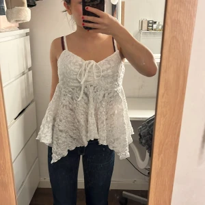 Vit spetslinne med knytband - Charmigt vitt linne med spetsdetaljer och knytband framtill. Toppen har smala axelband och en luftig passform. Man kan justera banden. Aldrig använd💕