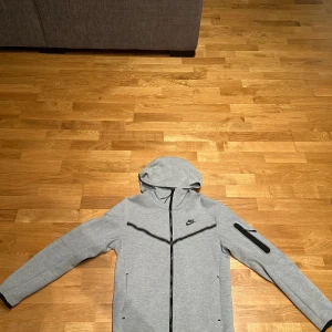 Grå hoodie från Nike - Grå Nike tech hoodie. Knappast använd, i nyskick. Storlek S.