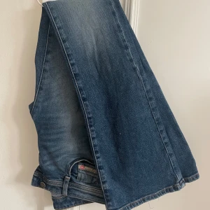 Blå jeans från Diesel - Snygga blå jeans från Diesel med klassisk femficksdesign och en bekväm passform. Perfekta för en avslappnad stil. Märkesdetaljer på baksidan ger en extra touch. Sönder i midjan men gör lätt att laga