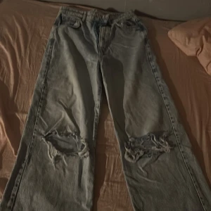 Ljusa jeans med slitningar - Säljer ett par ljusa jeans med coola slitningar på knäna. De har en klassisk femficksdesign och dragkedja. Perfekta för en avslappnad stil. Dom är lite uppklippta på benen så dom kan vara kanske en dm kortare men dom är stora och baggy ändå.