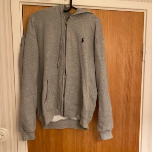 Grå zip-hoodie från Ralph Lauren - Säljer denna Ralph Lauren zip-tröjan eftersom den blivit för liten. Den är använd ungefär 1 år och är fortfarande i bra skick. Storlek L. Priset kan diskuteras.