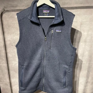 Patagonia fleeceväst - Säljer en snygg blå fleeceväst från Patagonia med dragkedja och en bröstficka. Perfekt för lager-på-lager under kyliga dagar. Västen har en stilren design med en liten logotyp på bröstet.