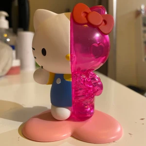 Hello Kitty figur - En unik Hello Kitty figur med en halvdel i klassisk design och den andra i genomskinlig rosa med hjärtformade detaljer. Figuren står på en rosa hjärtformad bas och har en röd rosett på huvudet.