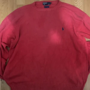 Röd stickad tröja från Ralph Lauren - Snygg röd stickad tröja från Ralph Lauren med rund halsringning och ett diskret logotypbroderi på bröstet. Perfekt för kyligare dagar.