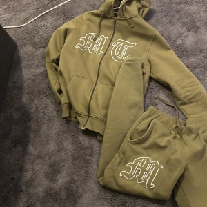 Olivgrön hoodie från tuttolente - Säljer en olivgrön hoodie från tuttolente med dragkedja och stor huva. Den har tryck med bokstäverna 'MT' på framsidan och en diskret design på baksidan. Perfekt för en avslappnad stil.