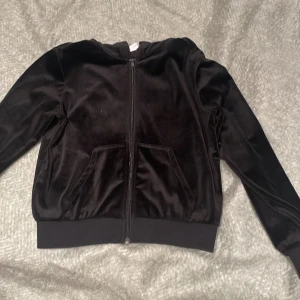 Svart velourjacka från Kappahl - Snygg svart velourjacka från Kappahl med dragkedja och huva. Jackan har långa ärmar och praktiska fickor framtill. Perfekt för en stilren look.