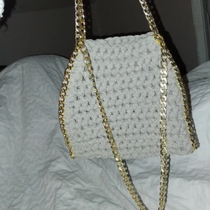 Grå virkad väska med guldkedja - Snygg grå virkad väska med en elegant guldkedja. Perfekt för att ge din outfit en unik touch. Väskan har en mjuk och mysig textur.