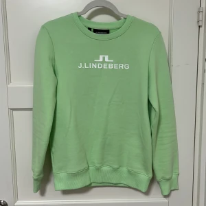 Ljusgrön sweatshirt från J.Lindeberg - Säljer en stilren grön sweatshirt från J.Lindeberg med deras logga tryckt på bröstet. Tröjan har en klassisk rund halsringning och långa ärmar. Perfekt för en avslappnad stil. Har aldrig använts, är för liten för mig tyvärr. Lappen är dock bortklippt. Storlek S