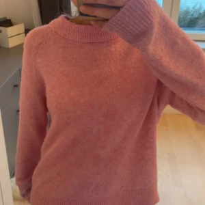 Rosa stickad tröja från Vero Moda - Mysig rosa stickad tröja från Vero Moda. Perfekt för kyliga dagar med sin mjuka och bekväma passform. Tröjan har långa ärmar och en rund halsringning.