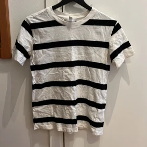 Randig t-shirt från H&M - Snygg vit och svart randig t-shirt från H&M i storlek XS. Perfekt för en avslappnad stil med korta ärmar och klassisk rund hals. Tillverkad i mjukt material för bekväm passform.