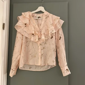 Blus med volang och blommönster - Detta är en fin oanvänd blus med volang och ett fint blommigt mönster, passar perfekt till våren och sommaren