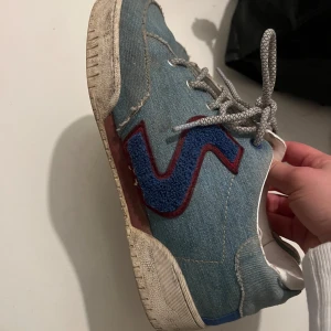 Blå sneakers från Stella McCartney - Snygga blå sneakers i jeansmaterial från Stella McCartney med röda och blå detaljer. Storlek 40. Använda men fortfarande fint skick. Finns vita skosnören som medföljer (ej original då de gick sönder) 