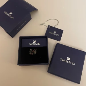 Swarovski brosch med svanmotiv - Elegant brosch  från Swarovski med ett vackert svanmotiv. Broschen är dekorerad med gnistrande stenar i svart och silver, vilket ger en lyxig känsla. Nytt skick och köpte för ungefär 1500