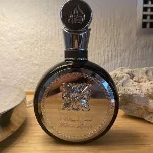 Lattafa Fakhar  - Elegant parfymflaska från Lattafa med en rund form och en lyxig silverfärgad etikett. 70ml kvar! Flaskan har en dekorativ design med ett detaljerat mönster och en stilren kork. Perfekt för den som söker en exklusiv doftupplevelse.