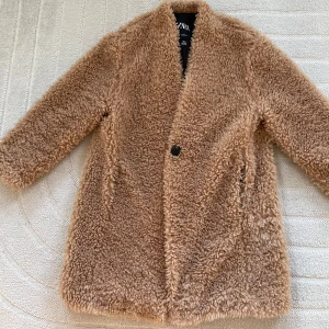 Beige teddyjacka från Zara M - Mysig beige teddyjacka från Zara med en enkel knapp framtill. Perfekt för kyliga dagar med sin fluffiga och varma design. Jackan har långa ärmar och en stilren look.