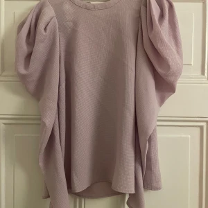 Ljuslila tröja från H&M - Säljer en ljuslila tröja från H&M med puffiga ärmar och en rund halsringning. Tröjan har en texturerad yta och är perfekt för en stilren look. Passar bra till både jeans och kjol.
