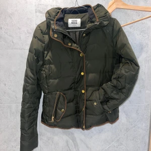 Grön pufferjacka från Vero Moda - Snygg grön pufferjacka från Vero Moda med dragkedja och knappar. Jackan har en hög krage och praktiska fickor med dragkedja.  Kan frakta