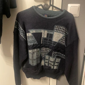 Mörkblå stickad tröja från Beyond Retro - Säljer en unik mörkblå stickad tröja från Beyond Retro med geometriskt mönster i ljusblått och grått. Tröjan har långa ärmar och en rund halsringning. Perfekt för en retrolook. bra skick oxh anvönt sparsamt. skulle säga liten i storleken 