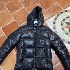 Save the duck jacka - Snygg svart save the duck pufferjacka med huva och dragkedja. Endast använd en vinter och skicket är i 8,5/10. Storleken är S men passar också M. Skriv vid mer frågor!