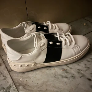 Valentino opens - Snygga vita sneakers från Valentino med svarta detaljer och nitar runt hälen. Skons snören är inte äkta eftersom de gick sönder men det går att köpa. Jag säljer dessa för att de inte passar mig. OBS PRISET ÄR INTE HUGGET I STEN och kan diskuteras. Det är lite rosa i skon men det går nog att tvätta bort och lite på sidan