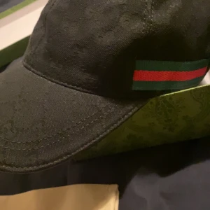 Svart keps från Gucci - Snygg svart keps från Gucci med det ikoniska gröna och röda bandet på sidan. Perfekt accessoar för en stilren look.