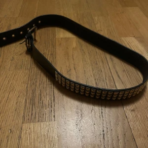 Svart nitat bälte - Coolt svart bälte med silverfärgade nitar. Perfekt för att ge en edgy touch till din outfit. Justerbar storlek med flera hål för bästa passform.