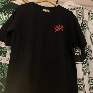 Svart t-shirt från Gallery Dept. - Snygg svart t-shirt från Gallery Dept. med röd text på både fram- och baksidan. Perfekt för en avslappnad stil.