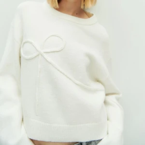 Vit tröja med rosettdetalj - Säljer en stilren vit tröja med en söt rosettdetalj på framsidan. Tröjan har en lös passform och långa ärmar, perfekt för en avslappnad look. Passar bra till jeans eller kjol för en chic outfit.