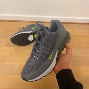 NIKE AIR MAX PULSE - Snygga grå Nike Air Max sneakers med limegröna detaljer och synlig luftkudde i hälen. Skorna har en sportig design med snörning och en bekväm passform. Perfekta för både träning och vardag. Skriv för mer info.