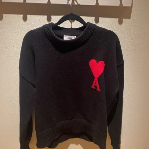 Svart tröja med rött hjärta från Ami Paris - Svart stickad sweatshirt med röd  ami paris logga. Säljer då den inte kommer till användning längre. Väldigt bra skick! Passar xs/s/m