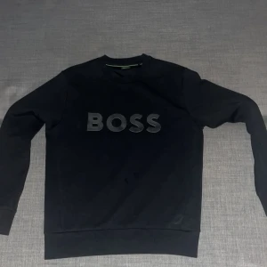 Svart sweatshirt från BOSS - Säljer en stilren svart sweatshirt från BOSS i storlek S men kan passa M. Tröjan har en klassisk design med BOSS-loggan i relief på framsidan. Perfekt för både vardag och avslappnade tillfällen. Den är i mycket bra skick och redo för en ny ägare!
