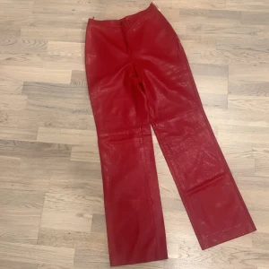 Röda byxor  - Snygga röda byxor i syntetmaterial/ kan vara skin med en glansig finish. De har en rak passform och stängs med knapp och dragkedja smal midja. Byxan har innefoder och är välsydda ” made in Italy” .Perfekta för en festlig look eller en utekväll. Byxorna är oanvända och redo att bäras med stil! 🍒