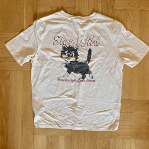 Retro krämfärgad t-shirt med kattmotiv - Cremefärgad t-shirt i retro-stil med kattmoriv på ryggen. Toppen är aldrig använd och är därför i nyskick. Passar stl S. Klicka gärna på köp nu och meddela för eventuella frågor. :)