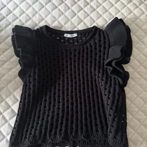 Svart stickad topp med volangärmar från Zara - Säljer en superfin svart stickad topp från Zara. Den har coola volangdetaljer på ärmarna och ett luftigt stickat mönster. Perfekt för både vardag och fest! 🖤