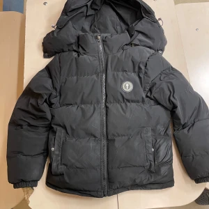 Svart pufferjacka från TRAPSTAR - Säljer en svart pufferjacka från TRAPSTAR i storlek XS. Jackan har en dragkedja framtill och en stor huva för extra värme. Den är perfekt för kalla vinterdagar, har digital kvitto