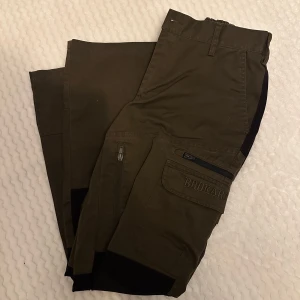 Gröna cargopants från Brokar - Säljer ett par gröna cargopants från Brokar i bra skick. Byxorna har flera praktiska fickor med dragkedjor och knappar, perfekt för vardagsäventyr. De är tillverkade i slitstarkt material och har en normal passform. Perfekta för höst och vår!