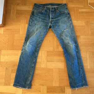 Levi’s 501 - Säljer ett par klassiska blå Levi's jeans i bra skick. De har en straight/slim passform med riktigt snygga slitningar och hål, som gör att byxorna sticker ut. Hör av er vid frågor eller funderingar!