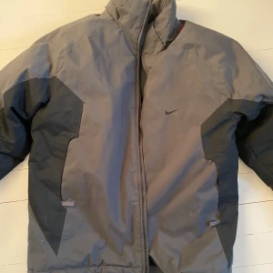 Nike grå vinterjacka - Varm vinterjacka från Nike, saknar ett strap band på ena sidan men inget som stör. Annars mycket bra skick