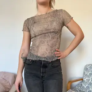 Säljer en snygg beige mesh-topp med korta ärmar och ett subtilt mönster. Perfekt för en utekväll eller fester. Toppen är tight och ger en stilren look. Passar bra till både jeans och kjol.