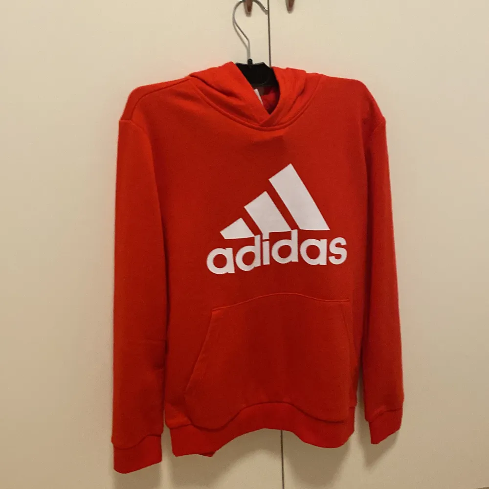 Säljer en snygg röd hoodie från Adidas i bra skick. Den har en stor vit logga på framsidan och en praktisk magficka. Perfekt för höst och vår, eller när du bara vill chilla hemma. Passar både för träning och vardag. Hör av dig om du är intresserad! 🔥helt oandvänd. Tröjor & Koftor.