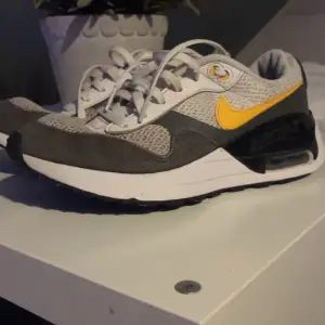 Säljer ett par snygga Nike air Max sneakers i grått och vitt med ett gult Nike märke. De har en bekväm passform och är perfekta för vardagsbruk. Skorna har snörning och är Använda men i bra skick, redo för nya äventyr! 🏃‍♂️