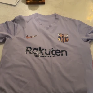 Ljuslila FC Barcelona tröja - Säljer en ljuslila FC Barcelona tröja från Nike. Den har korta ärmar och klubbens emblem på bröstet. Perfekt för alla Barca-fans! 💜