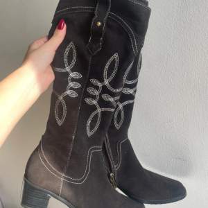 Svarta cowboy boots i mocka med vitt broderi. De har en låg klack och dragkedja på sidan för enkel på- och avtagning. Tecken på användning förekommer, i övrigt fint skick. Strl 36.