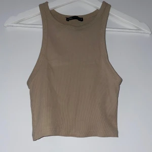 Beige ribbad linnetopp - Säljer en snygg beige ribbad linnetopp i storlek S men kan upplevas som Xs. Den är ärmlös och croppad, perfekt för sommardagar eller som ett lager under en jacka. Toppen har en enkel och stilren design som passar till det mesta. Perfekt för en avslappnad look!