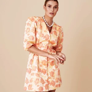 Blommig klänning från Adoore XS - Säljer en superfin blommig klänning från Adoore i ljusa toner av orange och beige. Klänningen har en kort längd och puffiga trekvartsärmar, perfekt för vår och sommar. Den har en v-ringad design och en figurnära passform som ger en elegant look. Perfekt för festliga tillfällen! 🌸